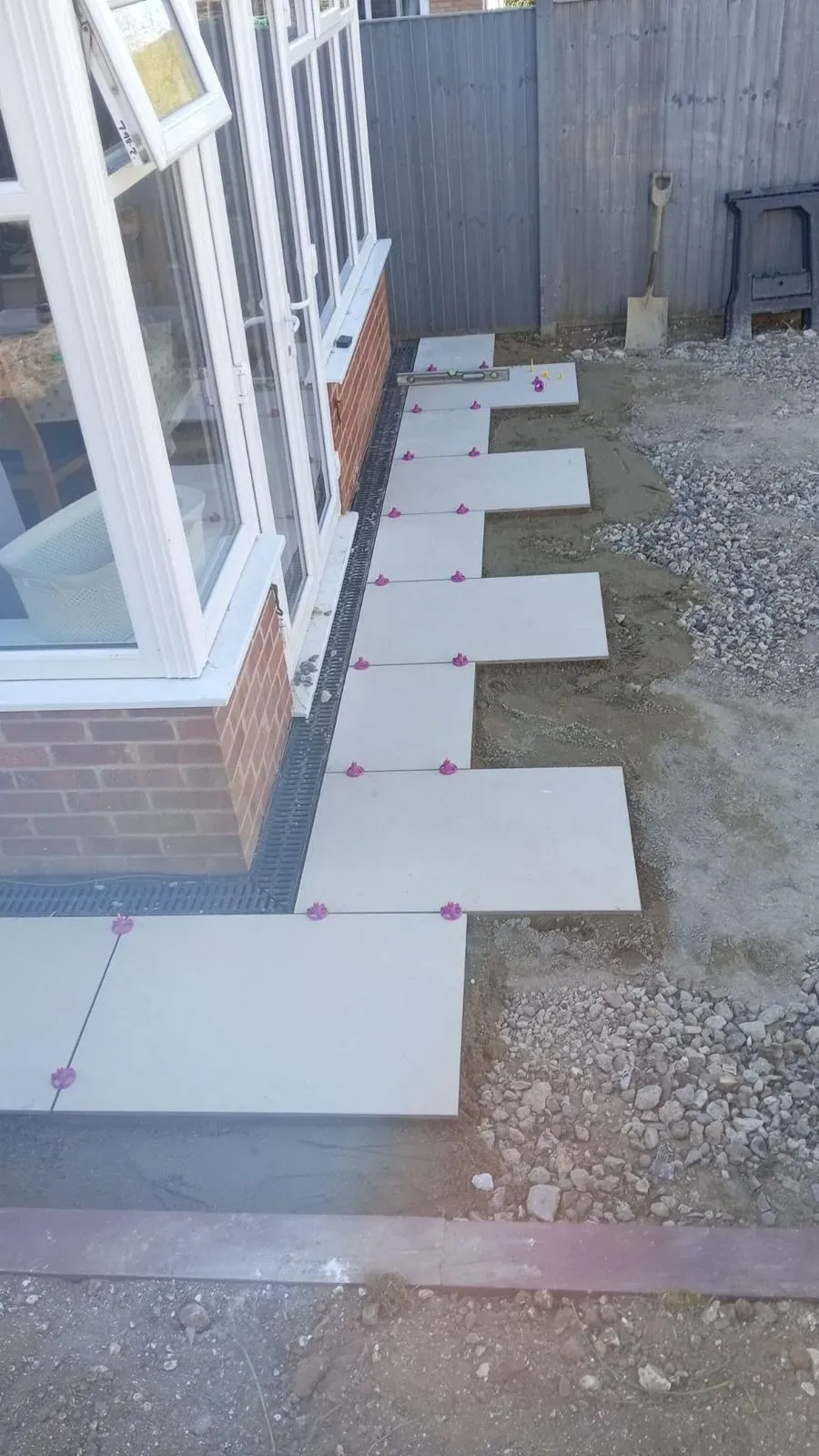 Paving slabs and linear drainage channel being installed next to a conservatory
