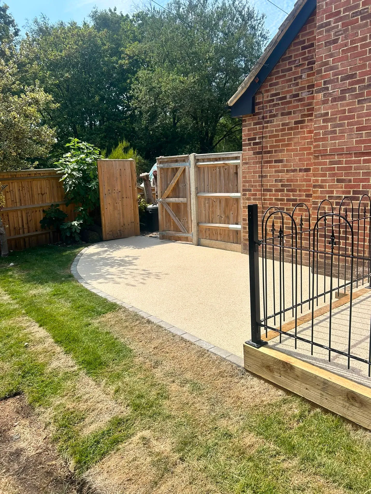 Permeable resin-bound surfacing with block paving borders and timber fencing installed beside a brick house