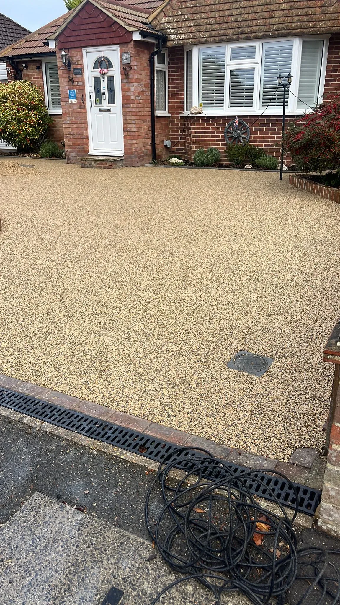 Newly laid light beige resin-bound driveway with linear drainage in front of a modern brick house in Tadley, Hampshire