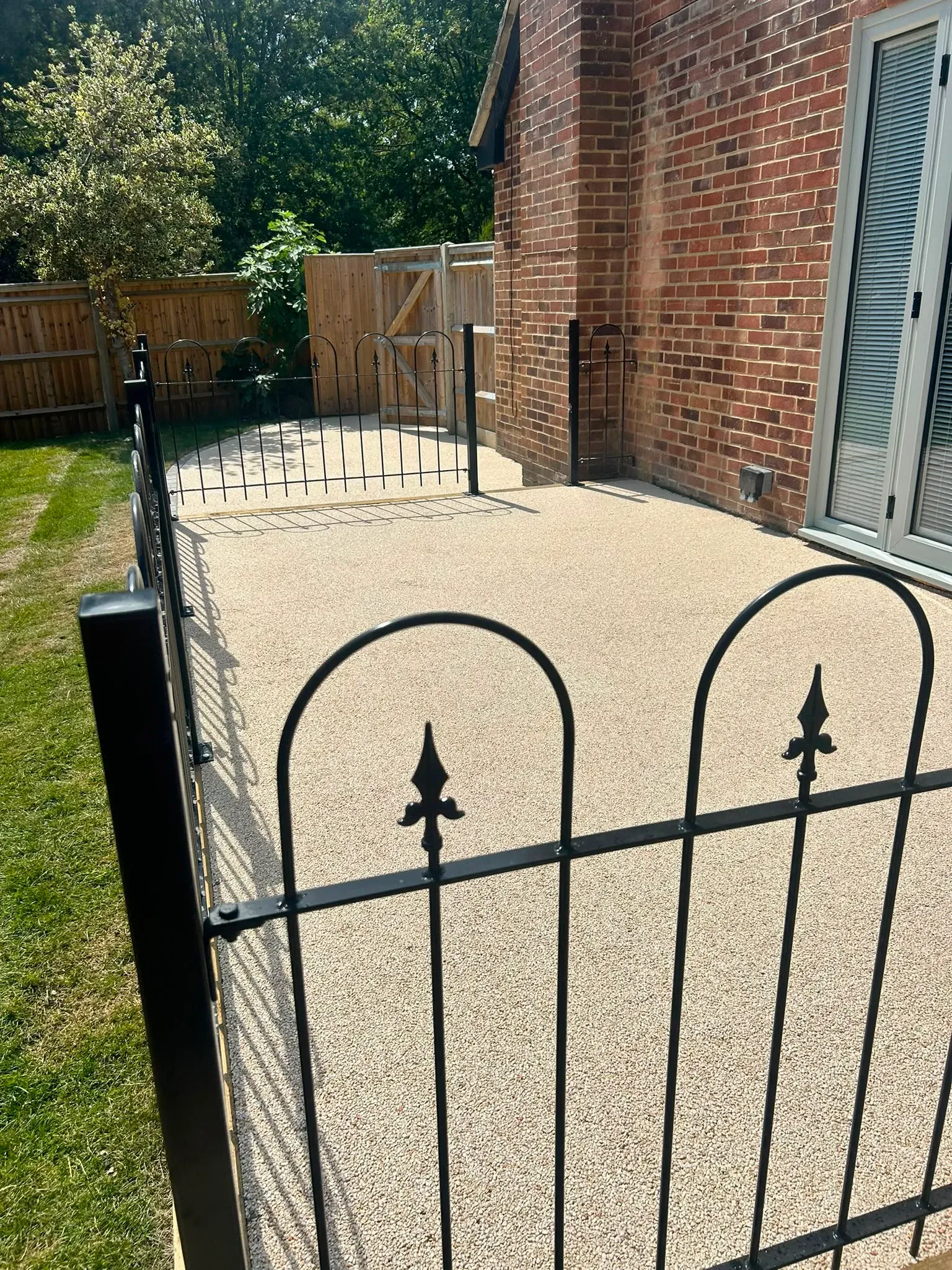 Resin-bound surfacing with decorative black metal boundary railings and timber fencing