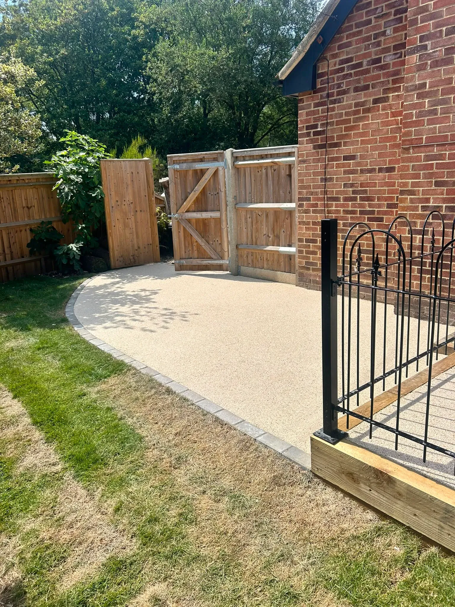 Permeable resin-bound surfacing with block paving edge restraints and timber boundary gate installed by River Vale (U.K) Ltd