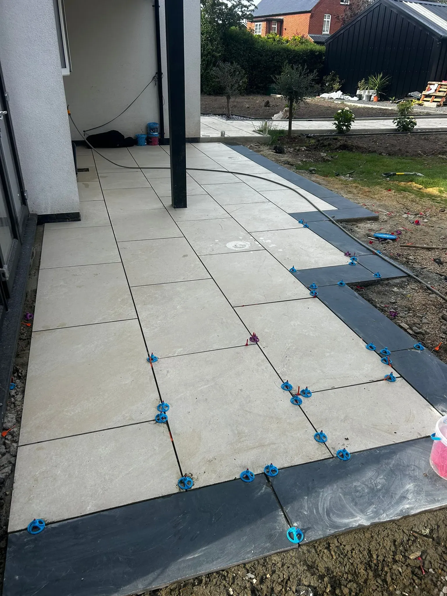 Porcelain patio slab installation in progress with levelling spacers and dark border tiles